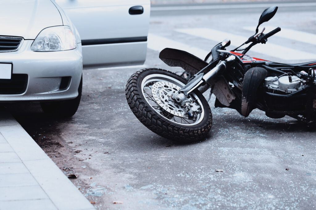 Motorcycle lying on the road and car standing with open door after the collision