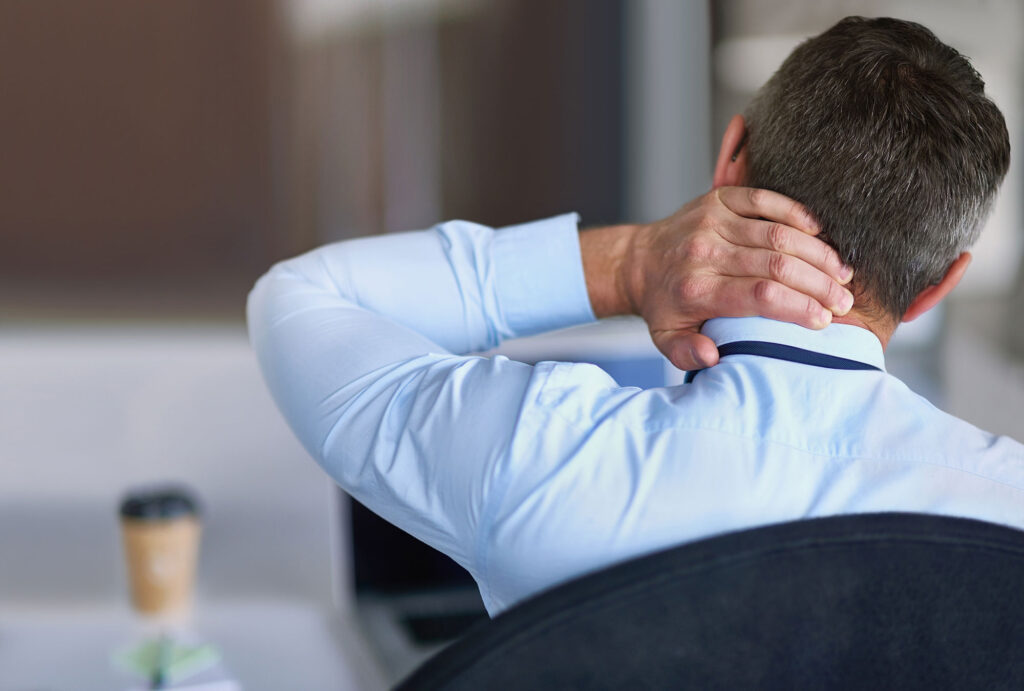A man seated in a chair and massaging his neck due to a workplace injury in the Philadelphia area