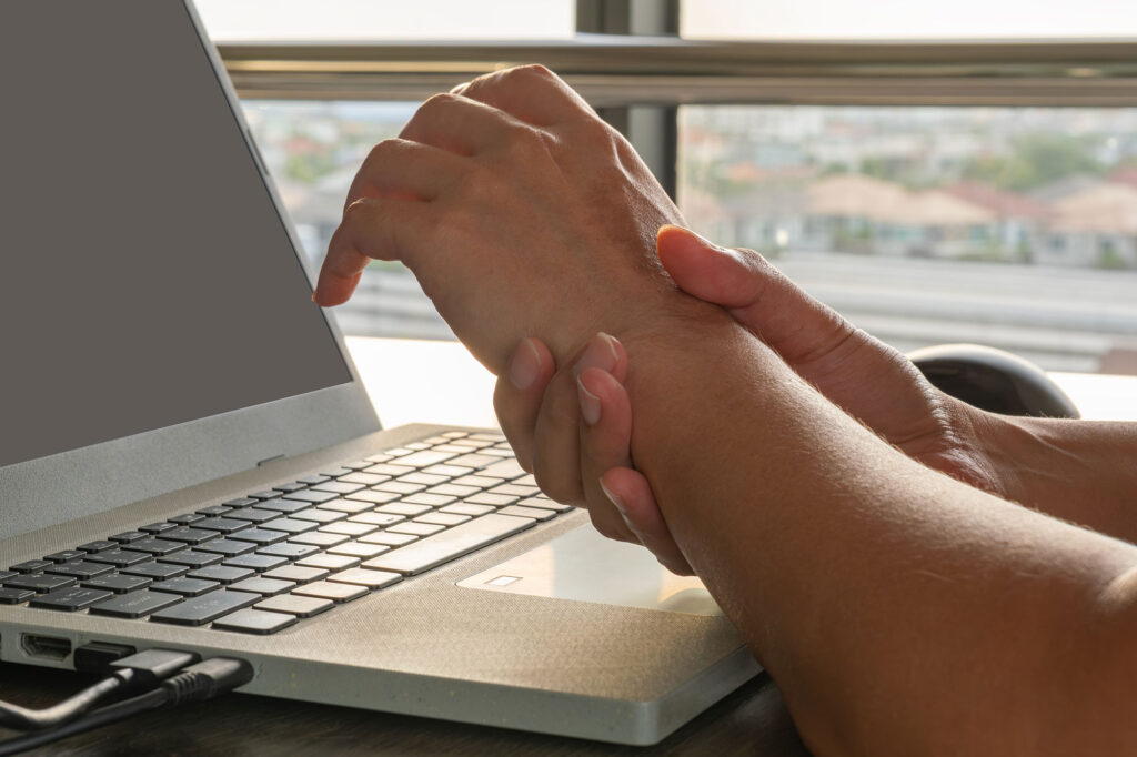 A woman holding her wrist while typing on her laptop due to a workplace injury in the Philadelphia area